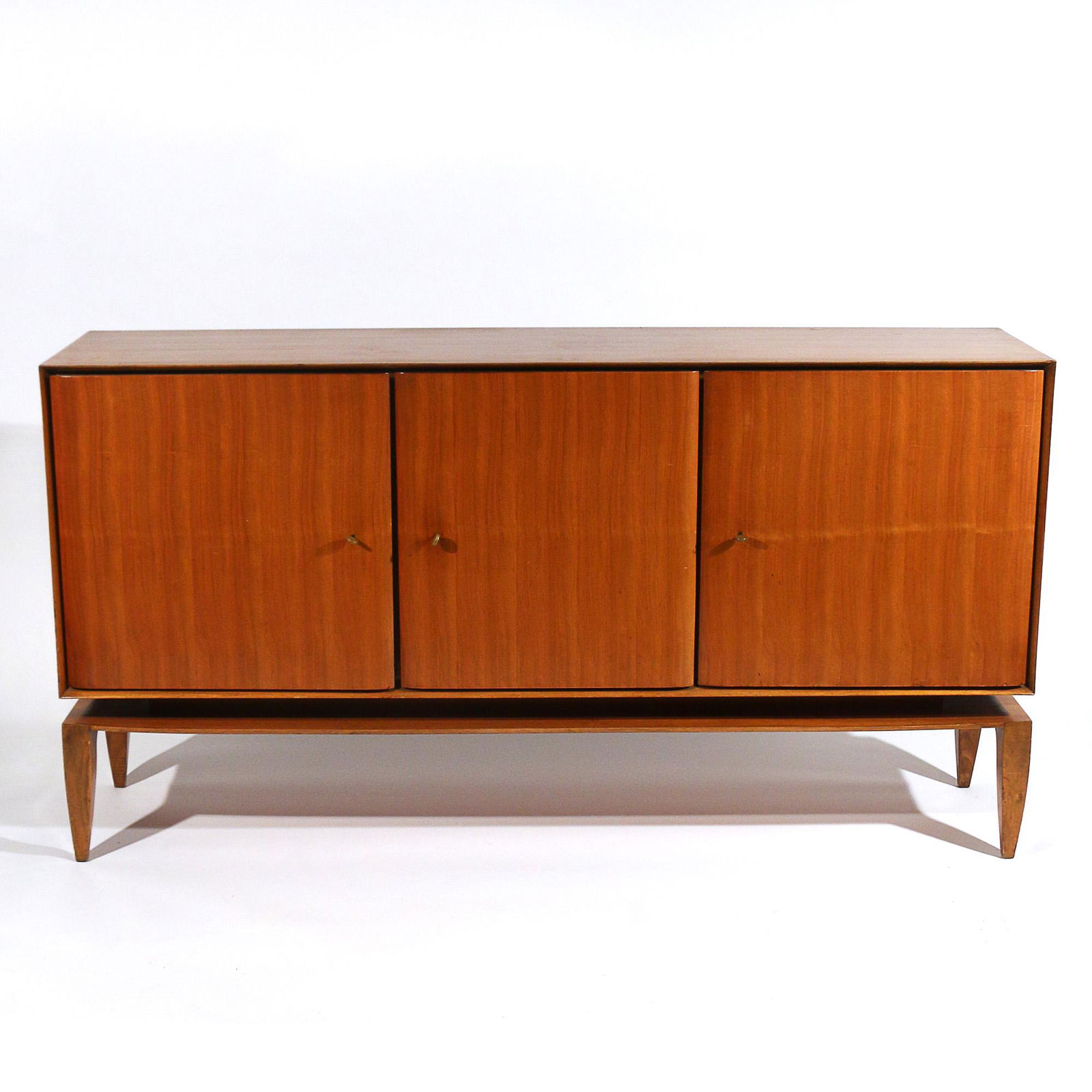 GIO PONTI (Italian, 1891-1979) SIDEBOARD, Mod. 1102: for M.Singer & Sons, Circa 1950s, sideboard cabinet having three figured wood doors, the two outer doors revealing interior shelves, the central cabinet door revealing a bank of four drawers, supporte