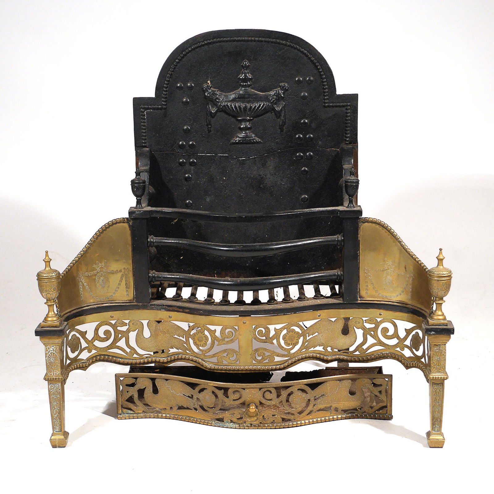 GEORGIAN IRON & BRASS FIREPLACE GRATE: Late 18th century, in the Adam style having serpentine front with conforming openwork brass apron, crested by wing etched sides, supported by square tapering brass etched legs crested by covered urns;