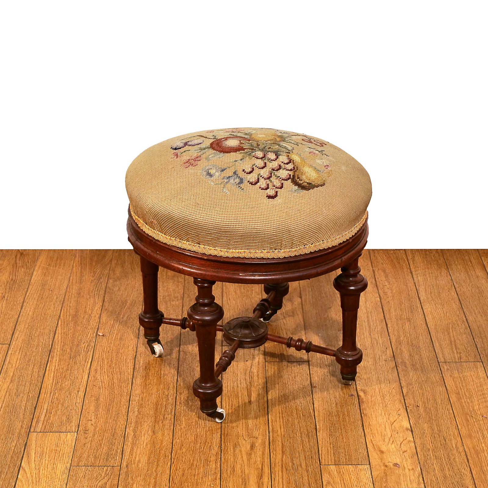 LATE 19th C. AESTHETIC FOOTSTOOL IN THE ROUND: the embroidered upholstery depicting fruit and flowers; on rubber casters, compass stretcher h. 16 x dia. 17 in. Provenance:items descended through an Old Greenwich, CT family