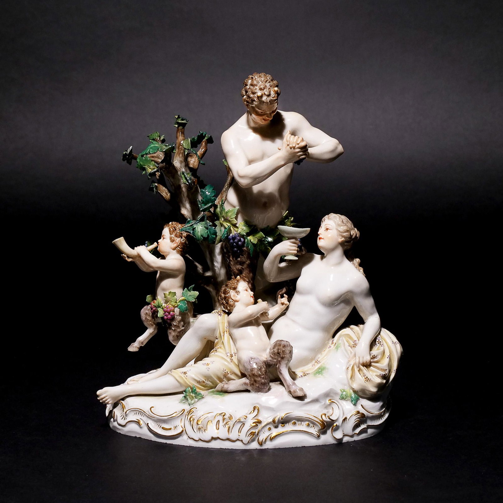 MEISSEN PORCELAIN BACCHANALIAN GROUP: 19th century, satyr squeezing grapes into goblet held by reclining nymph before a tree with fauns playing, incised on the bottom D63 / 122 with blue underglaze crossed swords mark h. 9-1/4 w. 8-1/4 d.
