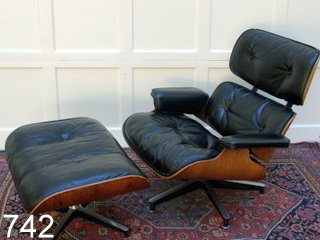 CHARLES EAMES LOUNGE CHAIR AND OTTOMAN: CHAIR MKD W/METAL TAB, COND.: LEATHER PIPING DMGD. AT CREST AND OTTOMAN W/DMGD. LEATHER SEAT, chair: h. 32", w. 32 1/2" (across arms) d. 39 1/2", ottoman: h. 17", 26 x 21"