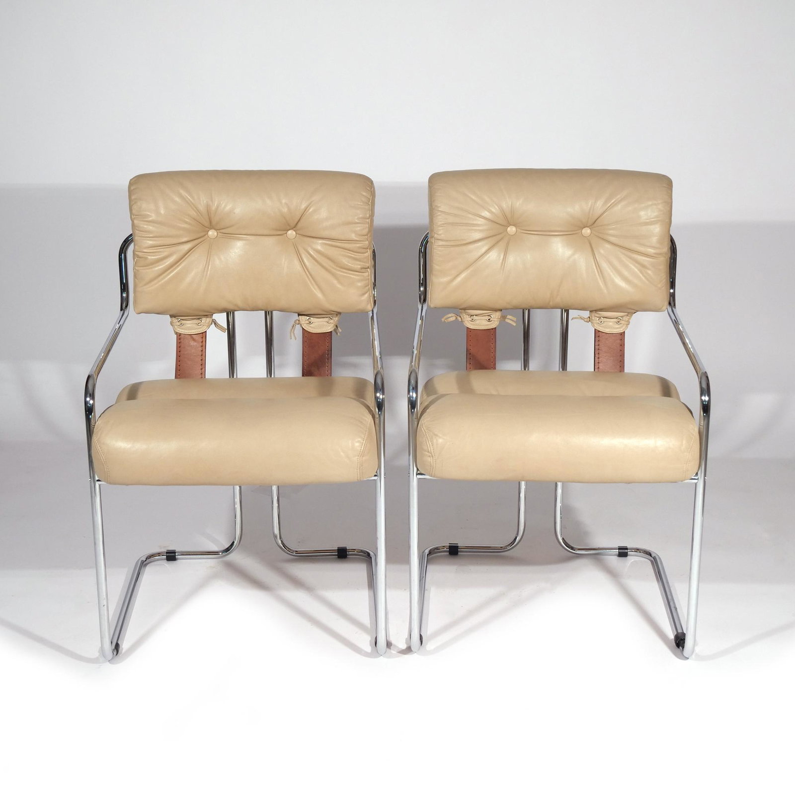 PAIR GUIDO FALESCHINI "TUCROMA" ARMCHAIRS: Mid-20th century, taupe leather tufted seats and backrests joined with tanned brown strap supports suspended from a chrome tubular steel frame h. 33 w. 21-1/2 d. 25 in. Provenance: Descended through t