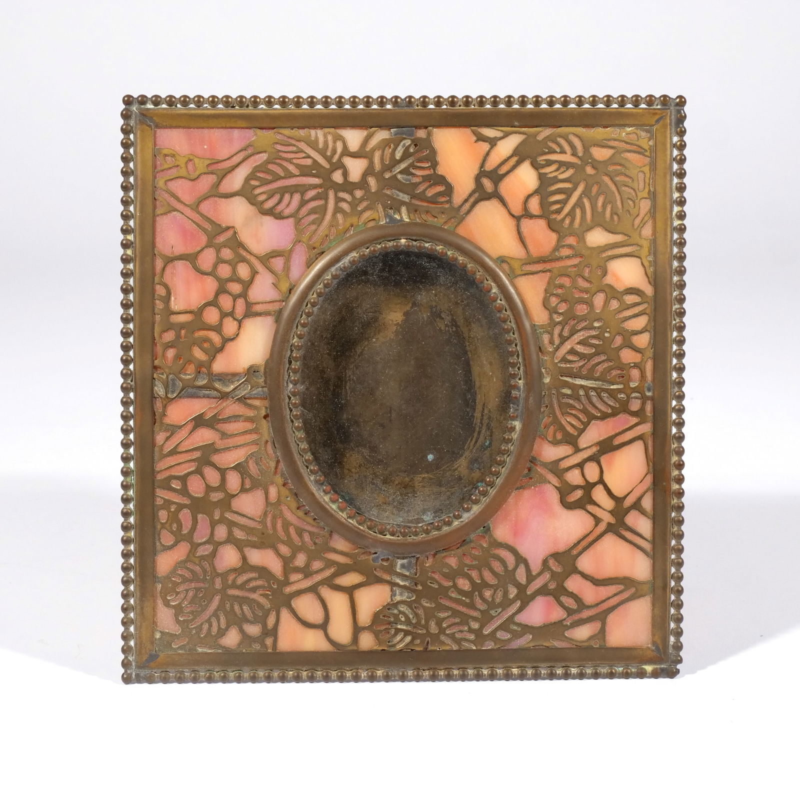 TIFFANY STUDIOS-STYLE RIVIERE FRAME: Pink slag glass under openwork brass with an oval insert (3-1/4 x 2-1/2 in.), stamped "RIVIERE STUDIOS / NEW YORK" on the back h. 7 w. 6-3/4 in. Provenance: A Greenwich, CT estate