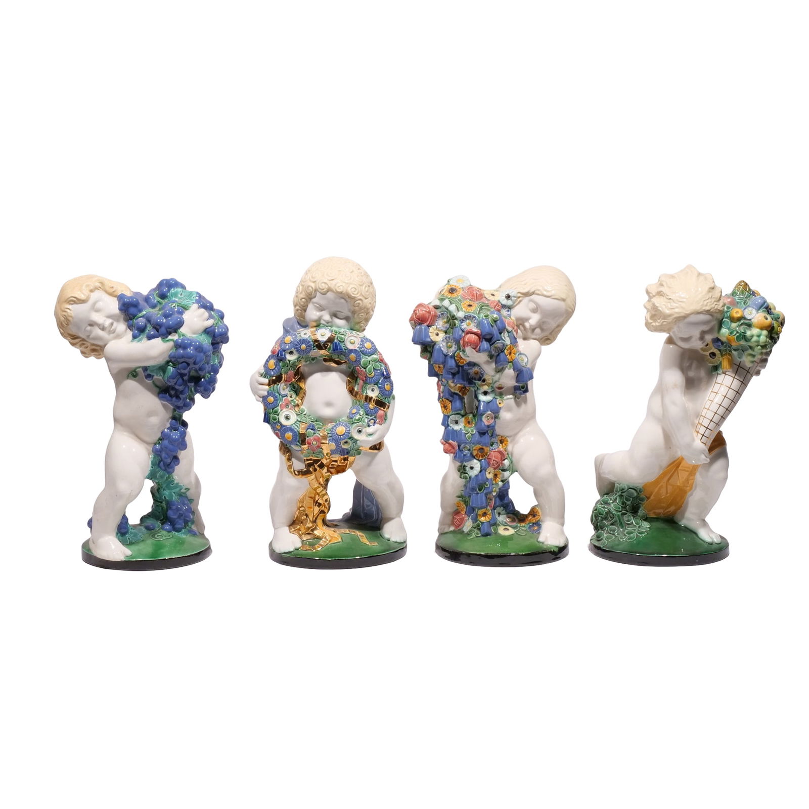 MICHAEL POWOLNY, "FOUR SEASONS" WIENER KERAMIK: An assembled set of four putti ceramic sculptures including a putto with cornucopia (Summer), a putto with flowers (Spring), a putto with grapes (Autumn), and a putto holding a wreath (Winter), made i