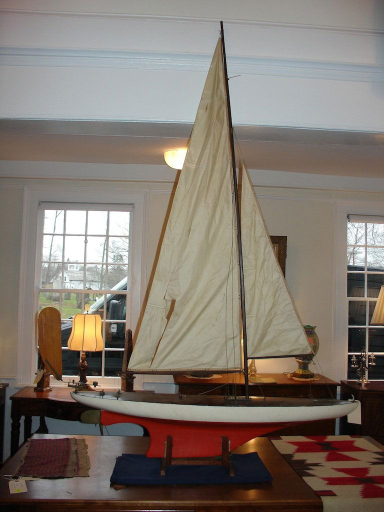 44 ) EARLY 20TH C POND BOAT W/STAND: POND BOAT MEASUREMENTS: BOAT BODY L:50". BOAT BODY WIDTH (AT WIDEST POINT):9.5". KEEL TO DECK H:10". MAST HEIGHT: 67". SAIL BOOM TO BOOM:33" COLORS: DECK:DARK BROWN. BODY:CREAM. KEEL: PUMPKIN ORANGE.