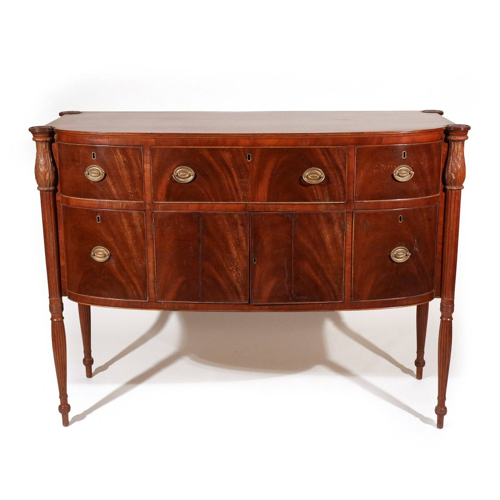 FEDERAL FLAME MAHOGANY BOWFRONT HALF SIDEBOARD: New York State, having outset carved corners with acanthus carving, over reeding terminating in bulbous peg feet h. 41-3/4 w. 55-1/2 d. 22-1/2 in. Provenance: The estate of late North Salem, N.Y. gent