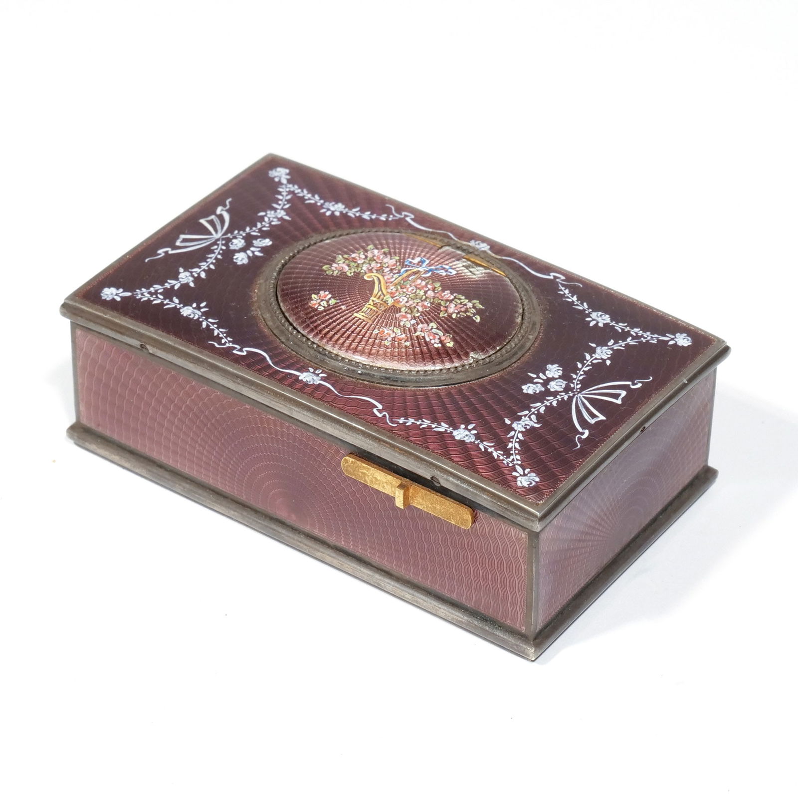 FRENCH ENAMELED SINGING BIRD AUTOMATON: Early 20th century, guilloche enameling showing a bouquet and French bow with laurel, on a wine-colored ground, marked 'Made in France', lacking a wind key h. 1-3/8 w. 3-7/8 d. 2-3/4 in. Provenance: A