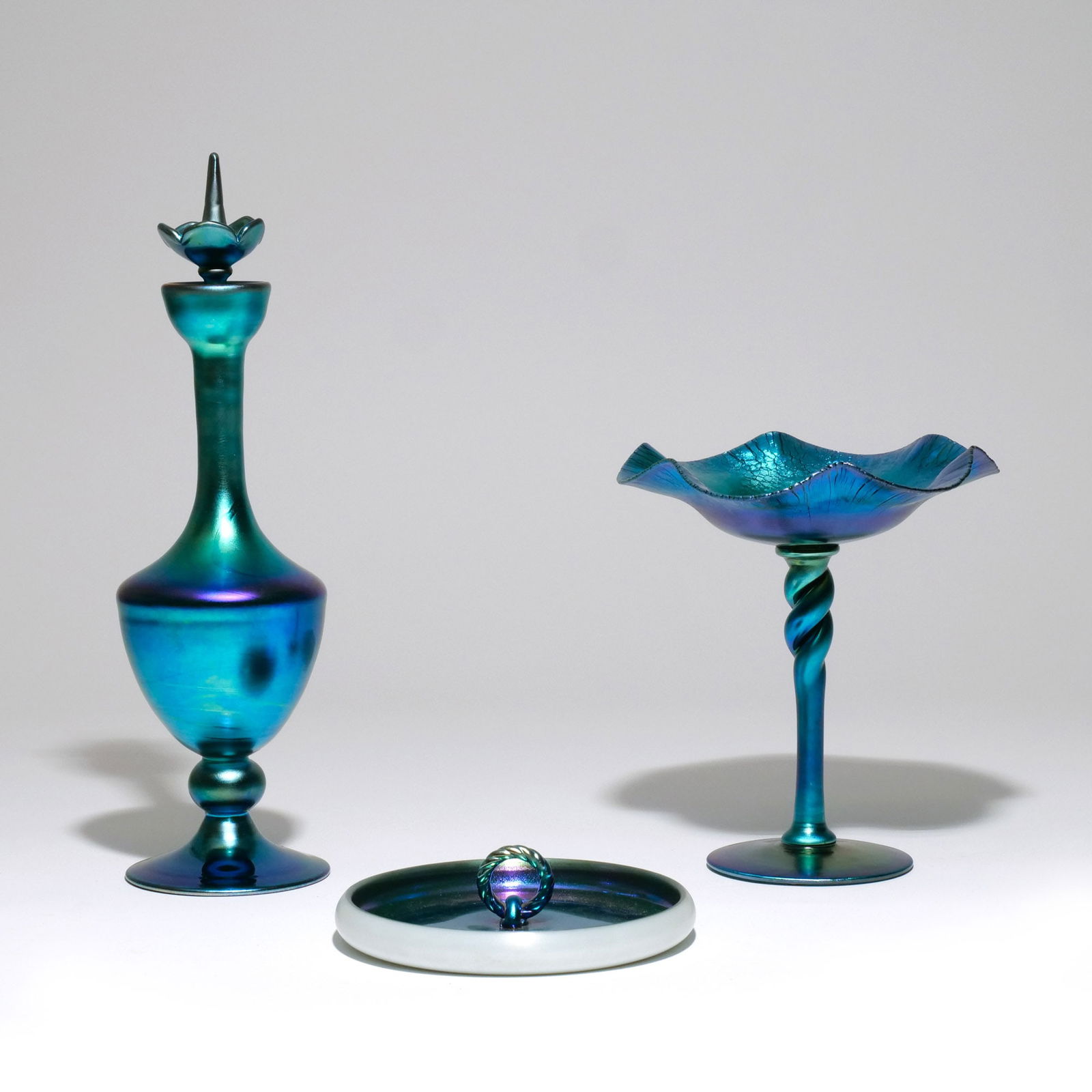 (3pc) STEUBEN BLUE AURENE GLASS: Circa 1920s, including a stoppered and footed bottle vase of baluster shape, signed 'Steuben Aurene 6047'; a compote with ruffled edge, signed 'aurene 367'; and an unsigned ashtray with rope loop hand