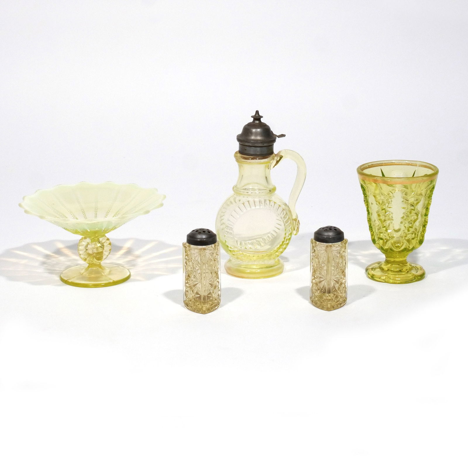 (5pc) ANTIQUE URANIUM GLASS: Including a compote / candy dish, a creamer with tin lid, a footed goblet, and a pair of shakers, all fluoresce under UV h. 7-1/2 in. (tallest) Provenance: Descent through the family of an Allendale,