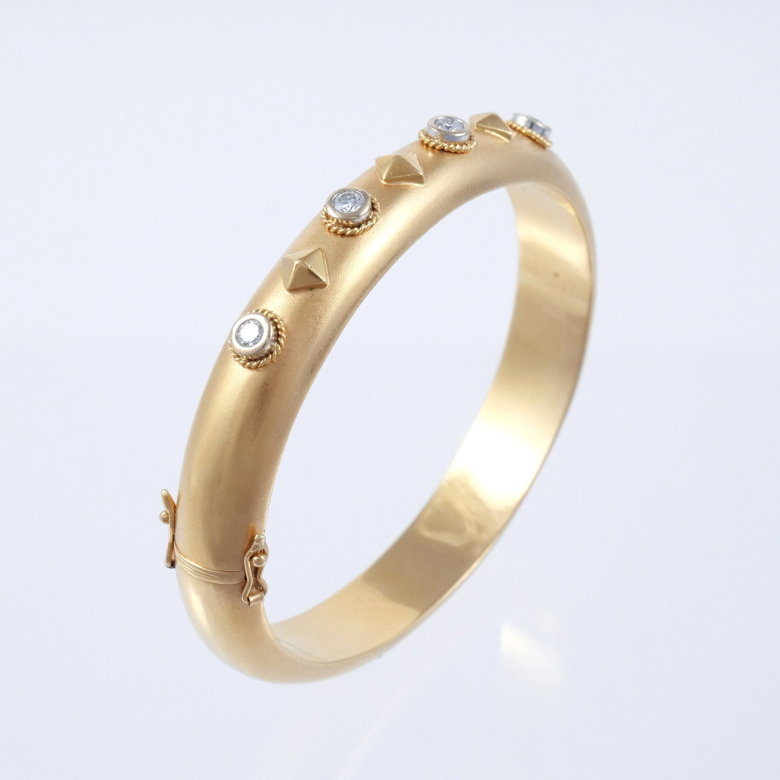 18K GOLD AND DIAMOND BANGLE BRACELET: Rounded matte gold with faceted bosses and 4 collet set round cut diamonds each approx. 0.15 cts, hinged closure, marked '750 / 18k' with possible maker's mark 'K', 6-1/2 in. interior circumference,