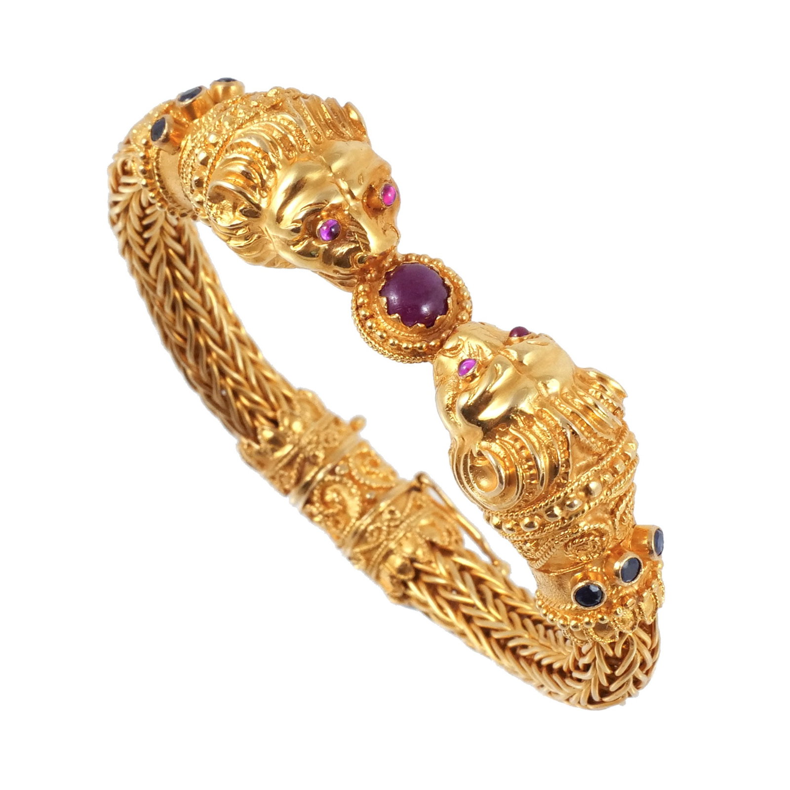 18K GOLD LION HEAD BRACELET: In the style of Lalaounis and Zolotas, designed as twin lion heads with bezel-set gemstone eyes and collar accents centering a cabochon gemstone, with applied granulation and wirework and a flexible