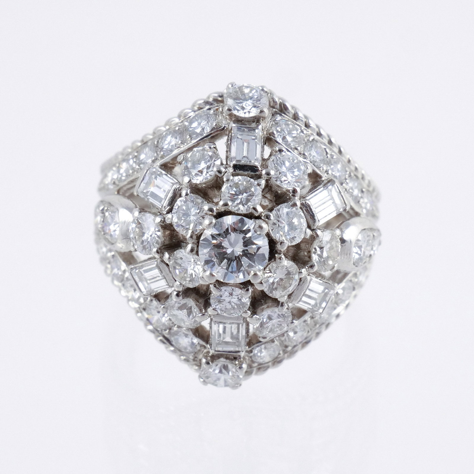 PLATINUM and DIAMOND RING of BOMBE SHAPE: With an approx. 0.4 ct center round brilliant surrounded by baguettes and other smaller round cut diamonds measuring approx. 2.75 cts total in a rope form platinum mount, size 6-3/4, 16.5 g total