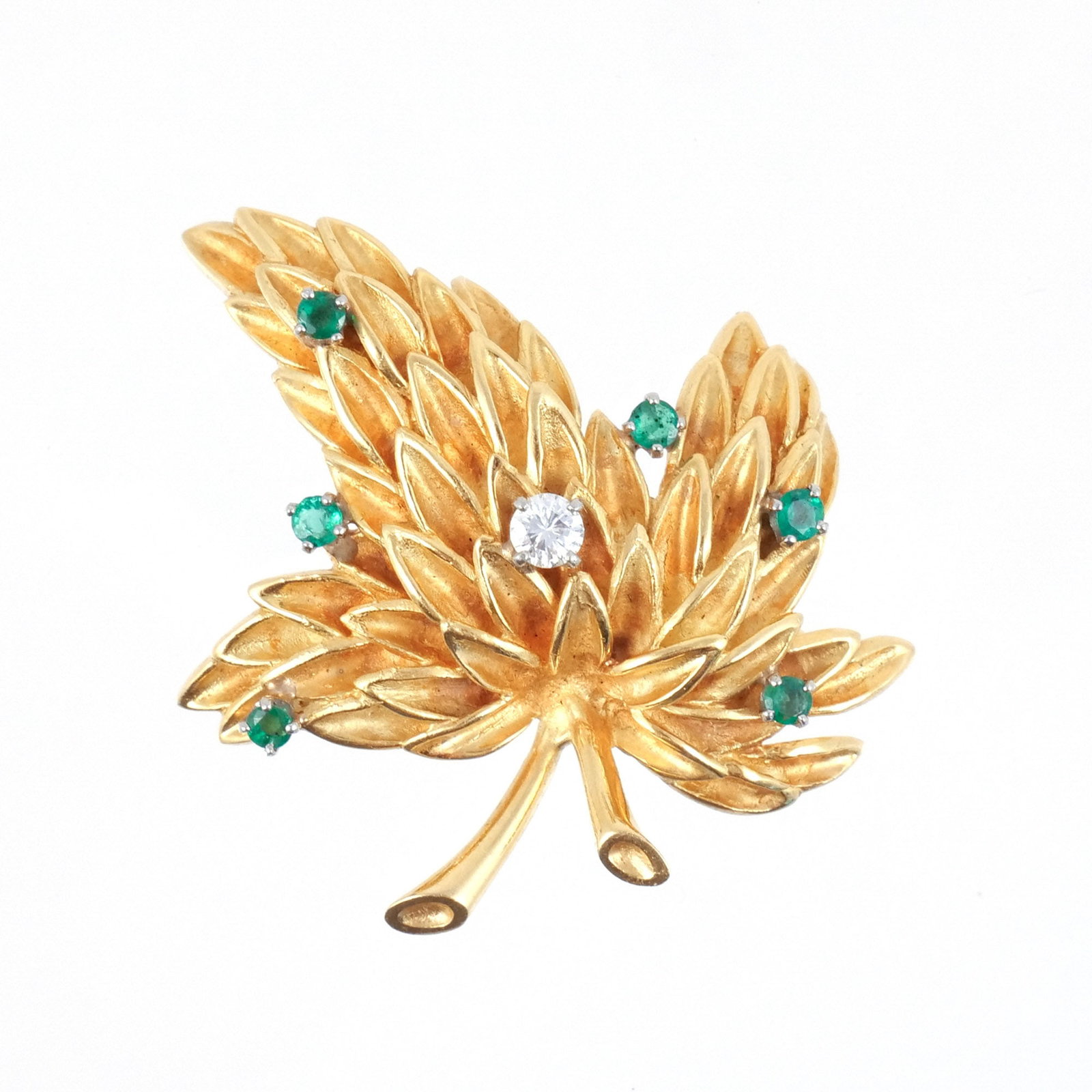 18K GOLD, DIAMOND, & EMERALD LEAF FORM BROOCH: Of matte and polished gold, centering an approx. 0.25 ct round diamond and accented by six 0.07 ct emeralds, marked '18k', 17.8 g total weight h. 1-1/2 w. 1-5/8 in. Provenance: Descent through the