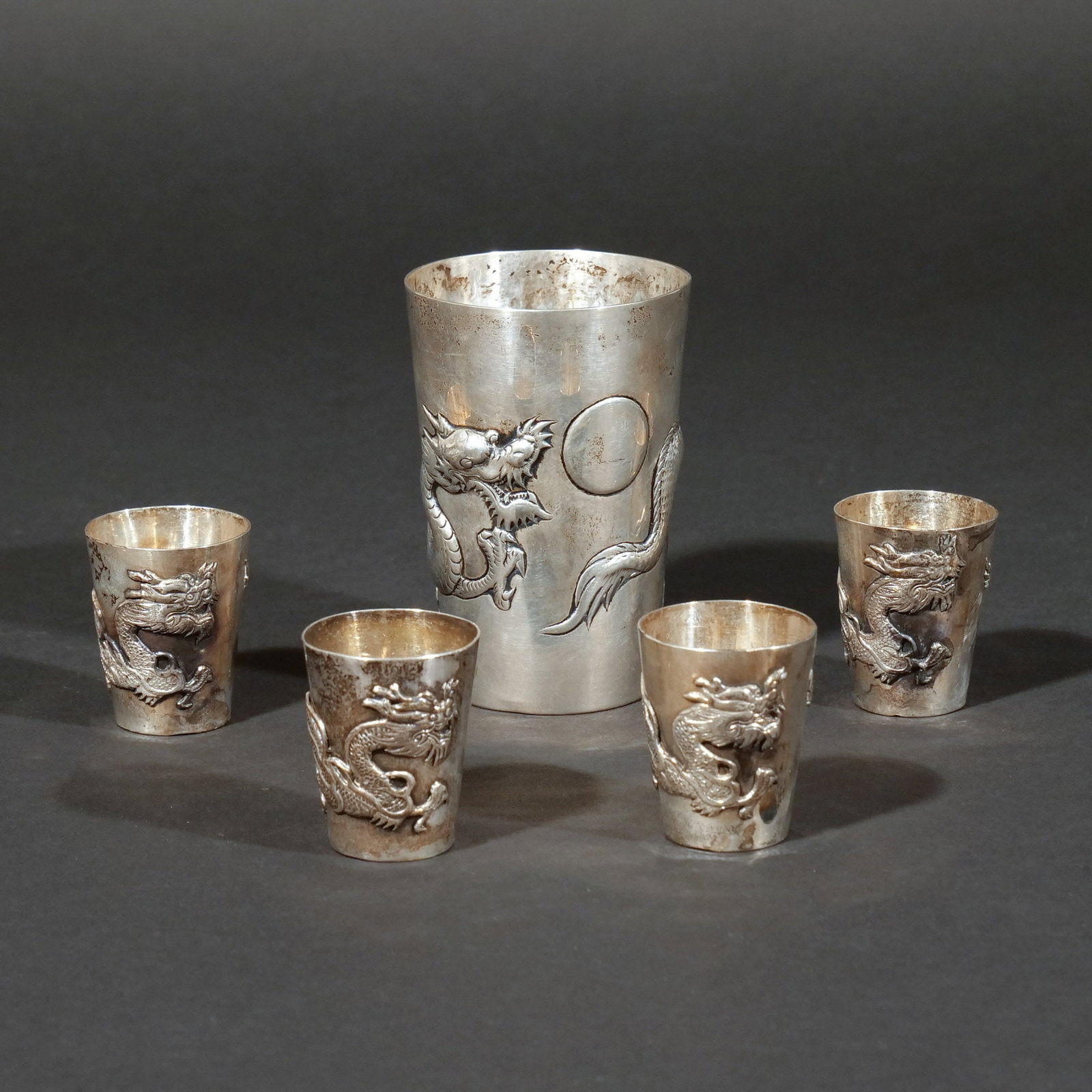 (5pc) CHINESE EXPORT SILVER BEAKER & SHOT CUPS: Likely by Cumshing, Canton, circa 1880, featuring detailed repouss? dragon motifs, the beaker with CS mark, 6.4 ozt total weight h. 4 in. (beaker) Provenance: Descent through a prominent Greenwich,