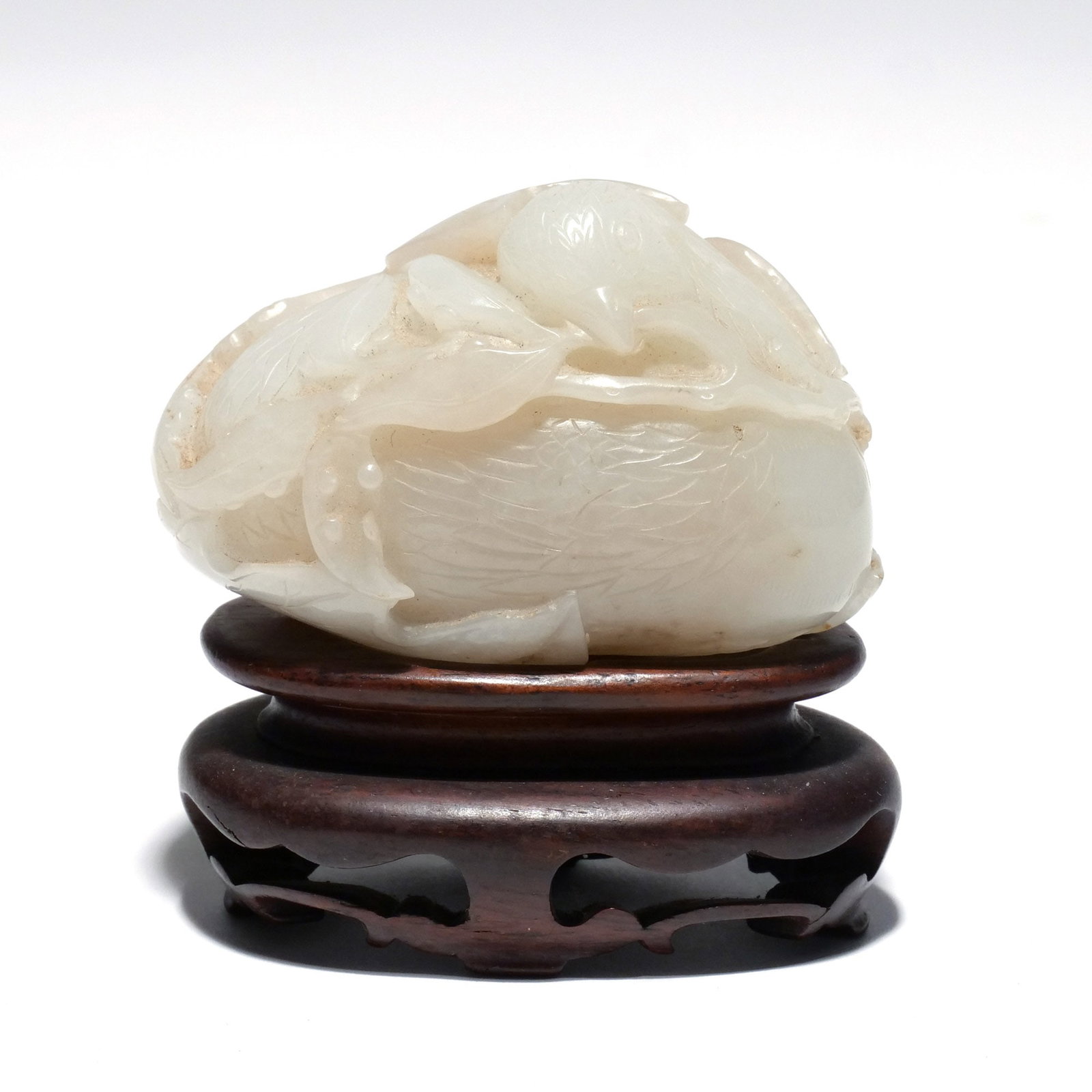 CHINESE CELADON JADE CARVED PEBBLE: Late Qing dynasty, 19th century, depicting a bird clutching a sprig, wrapped in a leaf h. 2 w. 3 d. 1-3/4 overall: 3 x 3 x 1-3/4 in. (with stand) Provenance: The estate of Richard and Jean M.