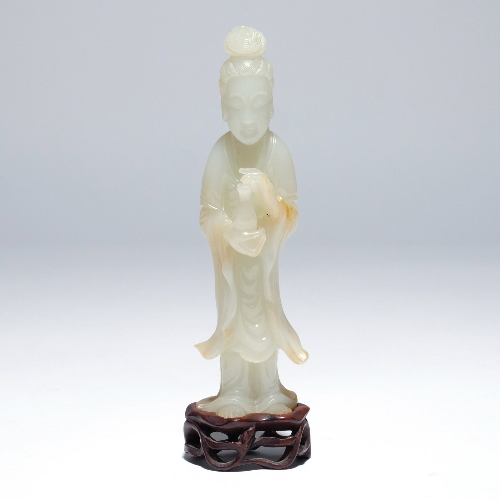 CHINESE WHITE/PALE CELADON JADE GUANYIN: The goddess of mercy depicted standing and holding her flask in both hands, on a wood base h. 5-1/2 in. Provenance: Descent through the consignor's grandmother's estate