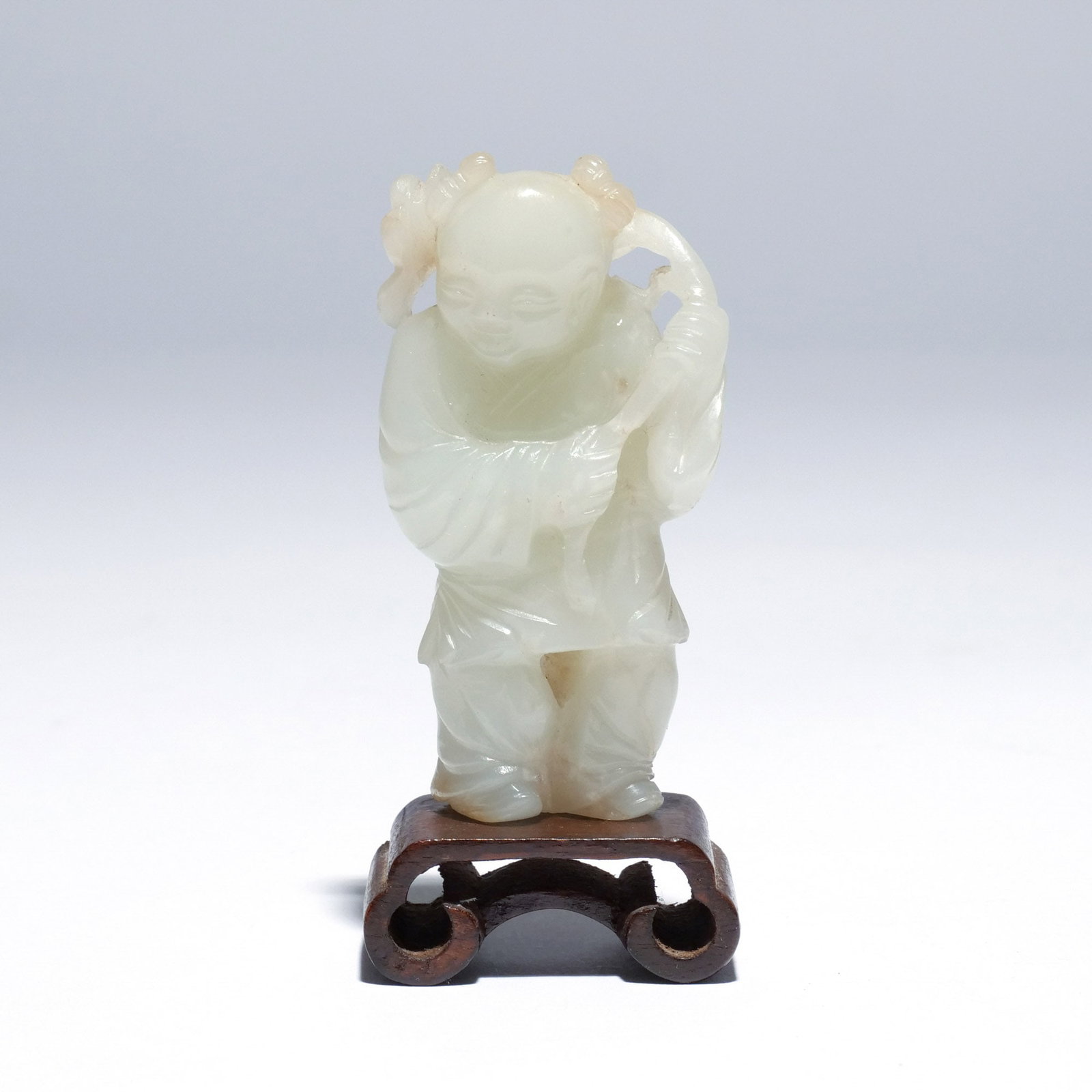 CHINESE PALE CELADON JADE FIGURE OF A BOY: Carved standing wearing a tunic and holding a large lotus stem in his hands, the stone of very pale celadon/white tone h. 3 in. Provenance: Descent through the consignor's grandmother's estate