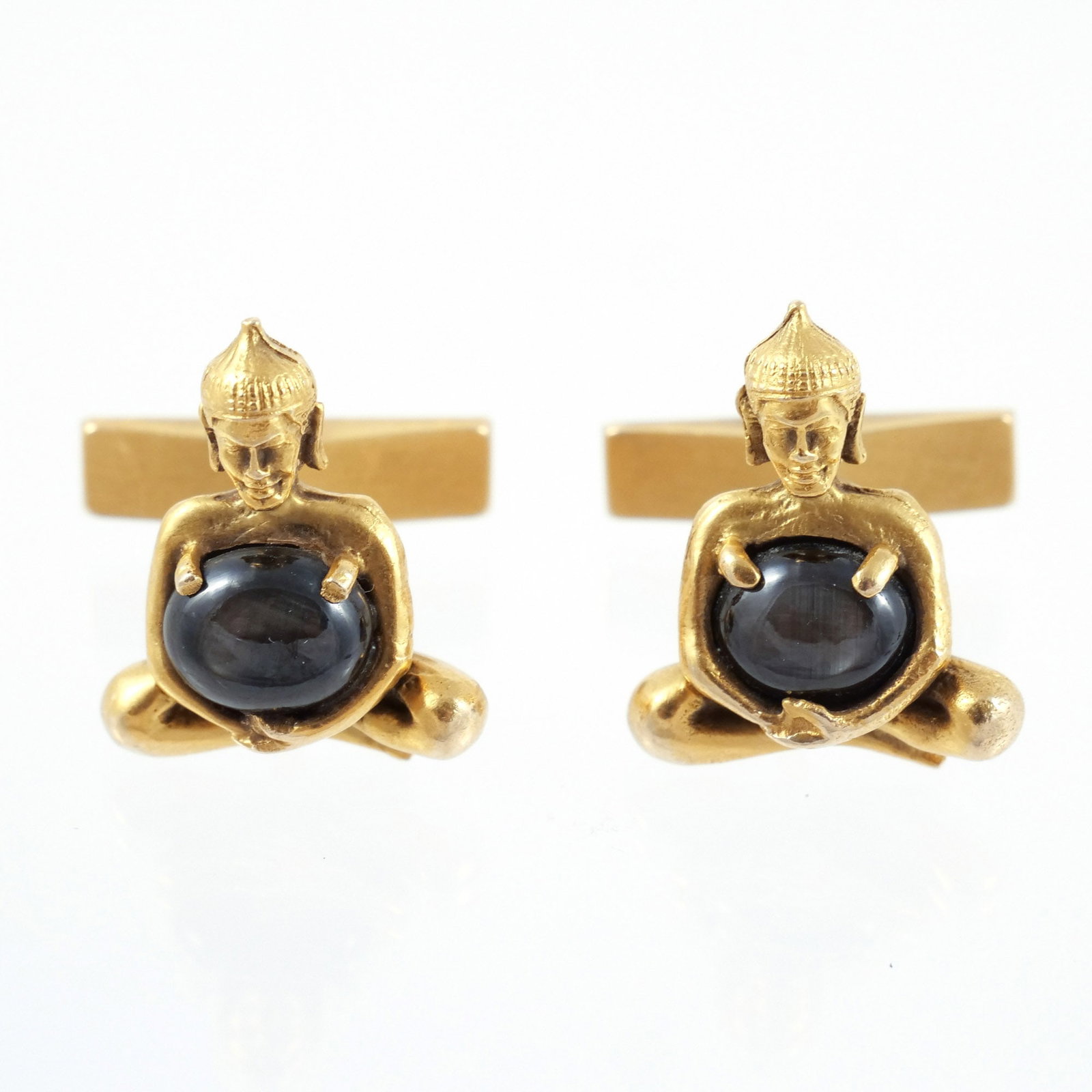 PAIR 14K GOLD and BLACK STAR SAPPHIRE CUFFLINKS: In the shape of a Buddha holding cabochon black star sapphires, each sapphire measuring approx. 9 x 6 mm, marked 14k, 16.5 g total weight h. 3/4 w. 5/8 in. Provenance: Descended through the estate of 