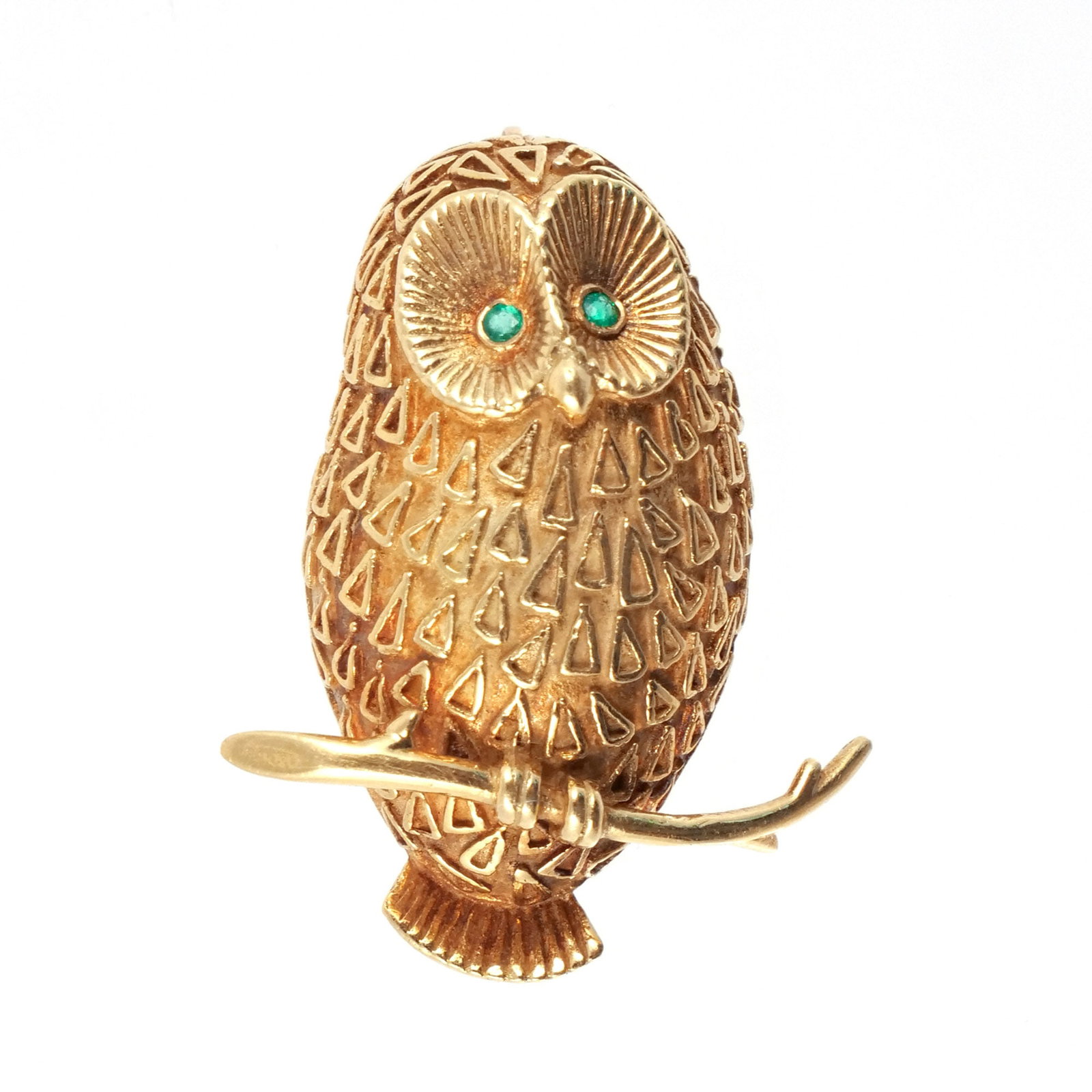 18K GOLD OWL FORM BROOCH: The owl of raised and fluted goal with small emerald eyes and seated on a branch, marked '18k', 9.6 g total weight h. 1-1/4 w. 1 in. (with branch) Provenance: Descent through the family of the current