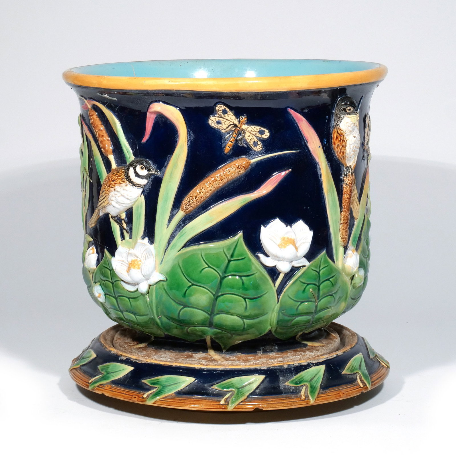 GEORGE JONES MAJOLICA JARDINI?RE AND STAND: c. 1870, molded in bas relief around the body with perched birds and insects amongst bulrush, underside with tortoiseshell glaze, marked with conjoined initials below crescent-shape device h. 14 w. 14