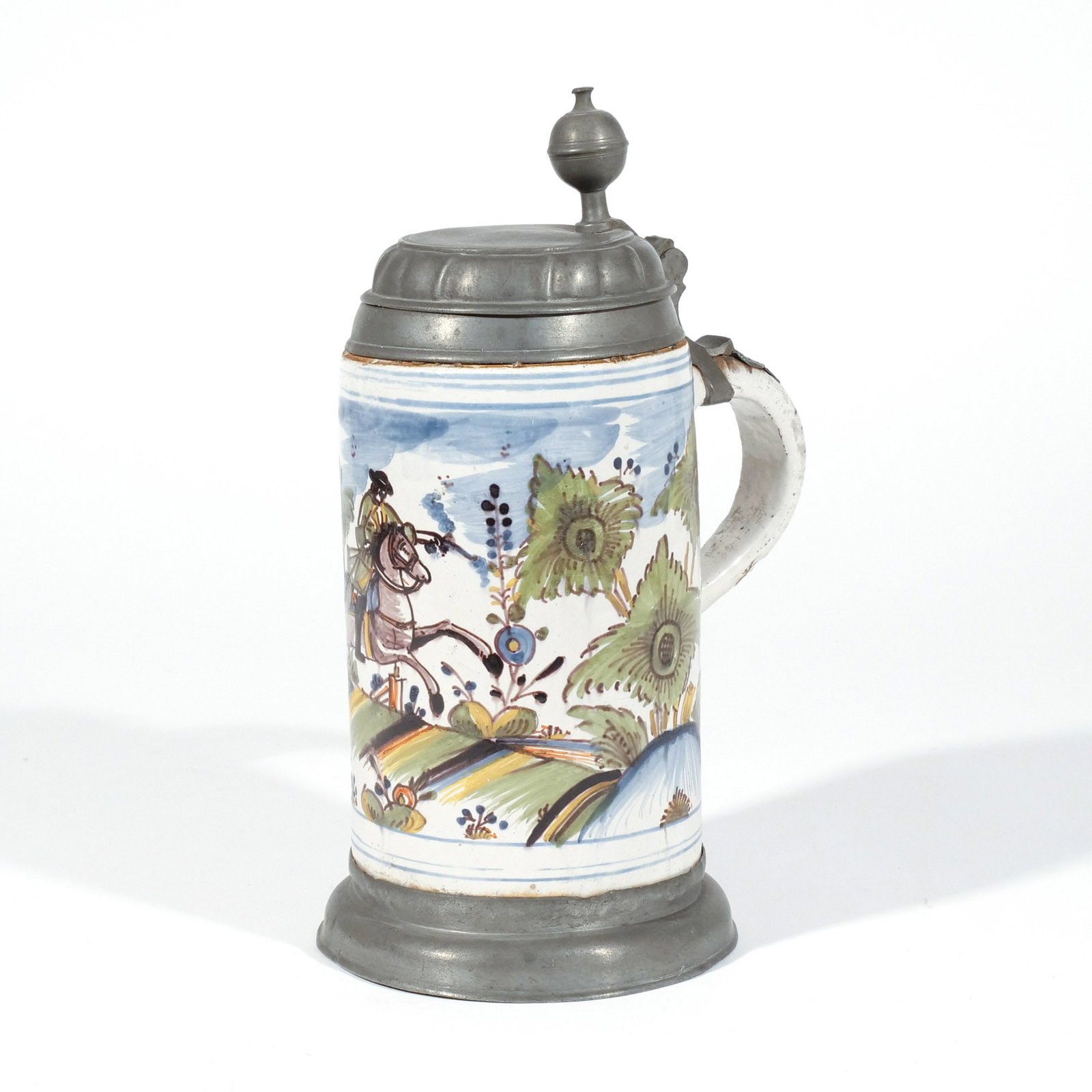 GERMAN FAIENCE WALZENKRUG STEIN with RIDER: Likely Thuringia, c. 1750, Buntmalerei decoration depicting a rider firing a pistol, with pewter cover and base h. 10-1/2 in. Provenance: The estate of a noted architect and bibliophile, Rye, NY