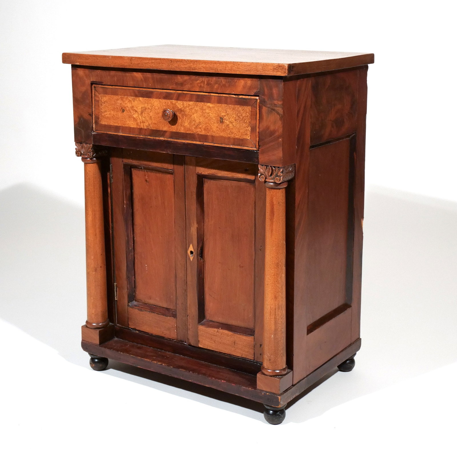 AMERICAN INLAID MAHOGANY & BURLWOOD COMMODE: 19th century, made in various woods, the rectangular top over a banded full drawer and a pair of cabinet doors flanked by engaged columns, all raised on ball feet h. 27-1/2 w. 21 d. 14-1/2 in.