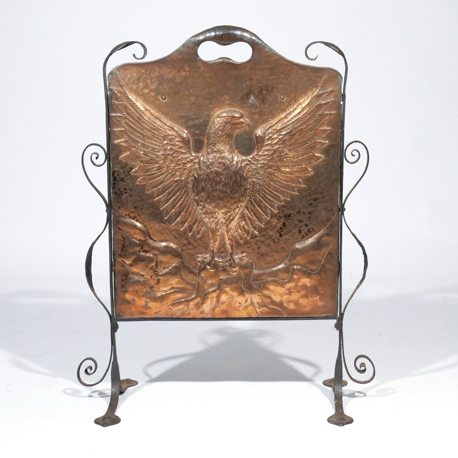 ARTS & CRAFTS HAMMERED COPPER FIRE SCREEN: Early 20th century, depicting an eagle with outspread wings en repousse, with wrought iron surround h. 30 w. 18-1/2 in. Provenance: Private collection, Bernardsville, NJ [In Situ Item] This item will