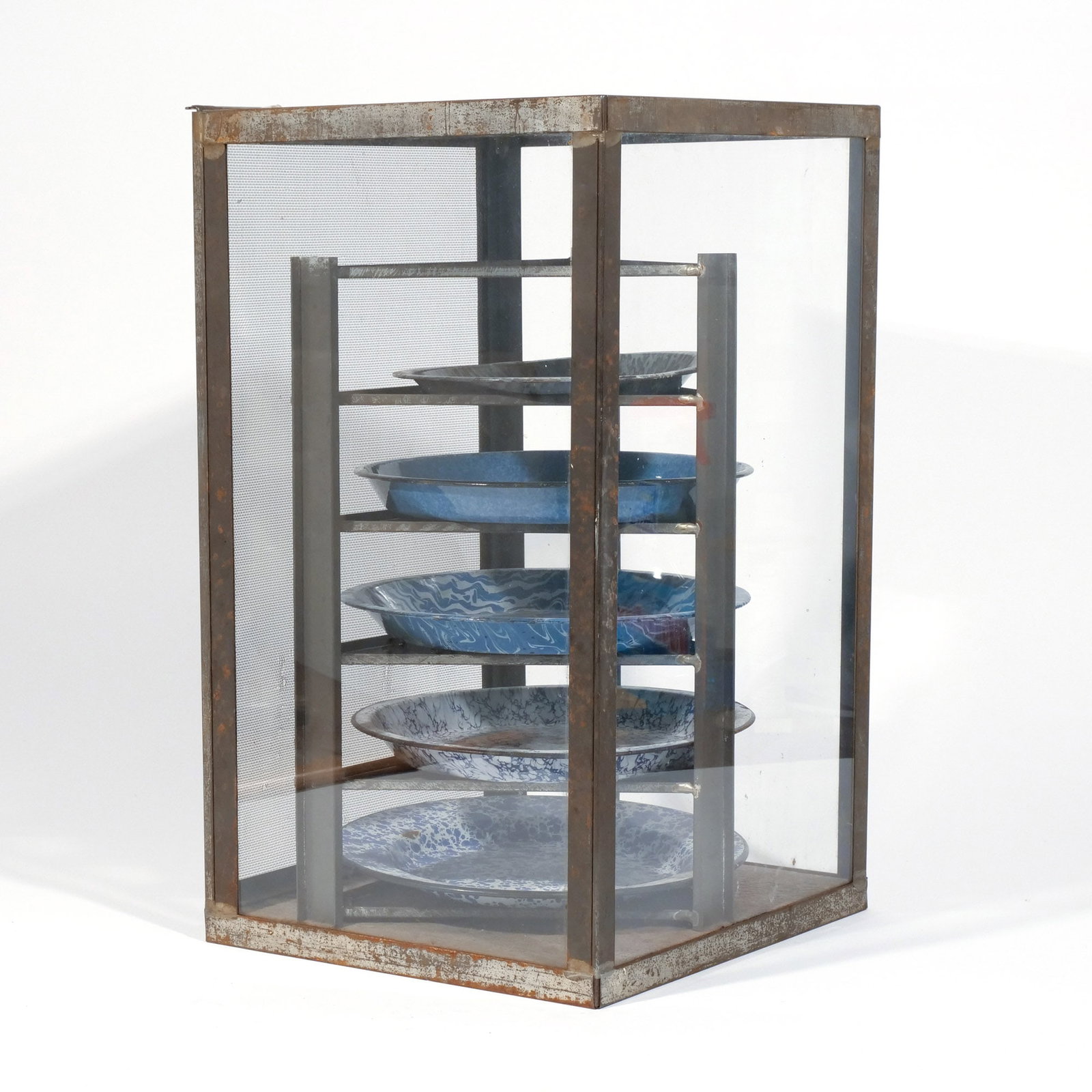 AMERICAN COUNTRY TABLETOP PIE SAFE: Early 20th century, the 7-tier pie safe made of tin with three glass sides and a screen door; sold with 5 enameled metal pie dishes with marbled and other decoration h. 20 w. 12 d. 12-1/2 in. Provenan