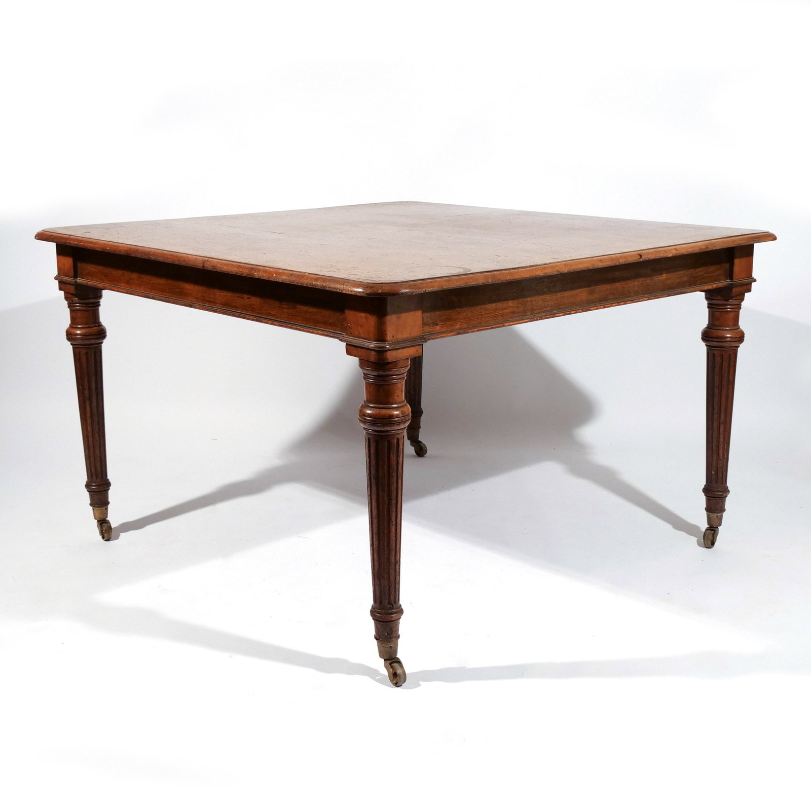 AMERICAN OAK SQUARE DINING TABLE: Late 19th / each 20th century, featuring tapered round fluted legs ending in casters, two board top h. 29 w. 48 d. 48 in. Provenance: The estate of noted artist and author Edward Giobbi (1926-2026),