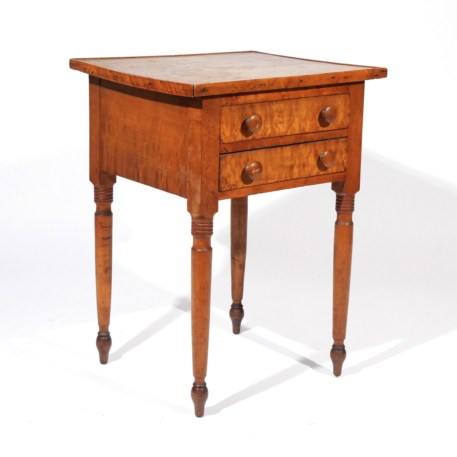 AMERICAN FIGURED MAPLE TWO-DRAWER STAND: 19th century, with one-board top and two drawers over ring turned legs ending in peg feet h. 28 w. 21 d. 17-1/2 in. Provenance: Private collection, Bernardsville, NJ [In Situ Item] This item will not