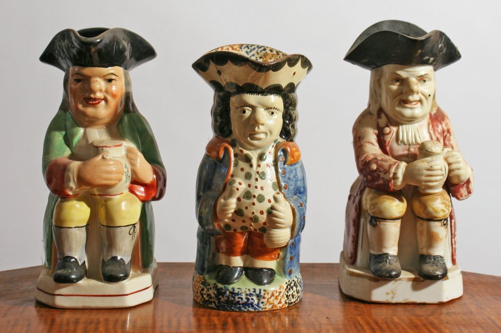 301) 3 STAFFORDSHIRE TOBY MUGS, one standing with: a blue overcoat having an orange collar, one seated with a green jacket and yellow leggings, and one with a worn red jacket and yellow leggings, Height range: 8 ¼ - 7 ¾", one with damage to hat
