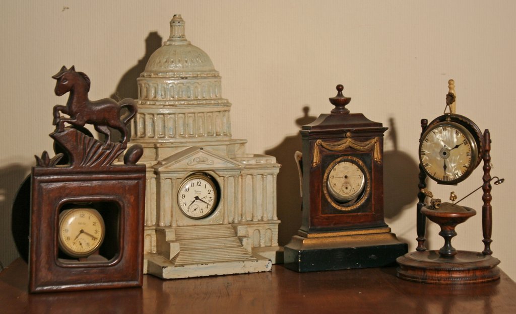 371) 4 WATCH HUTCHES: one in cast iron of the: Capitol building, H: 9 ½", one carved wood crested with a horse, one in the form of a bracket clock with Lincoln drapery, and the last with a turned fount and spindle sides