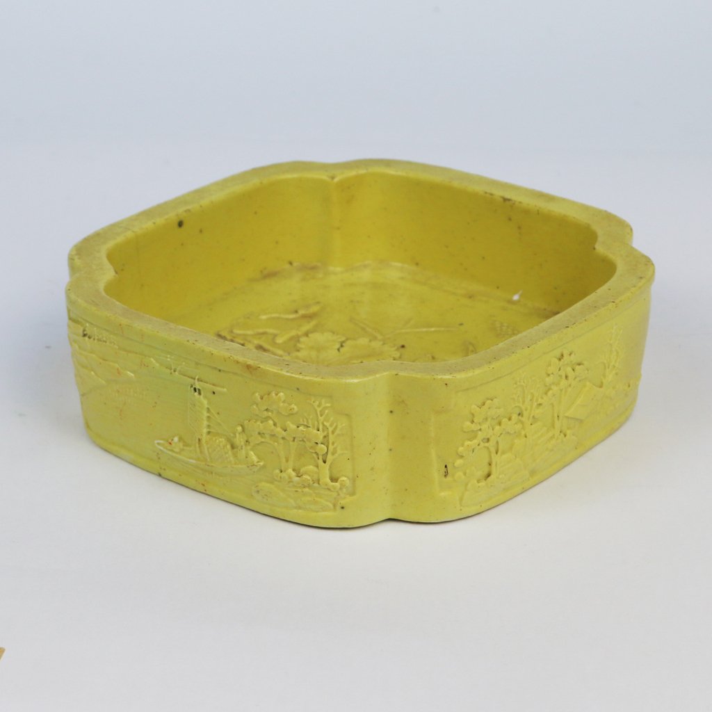 CHINESE GLAZED EARTHENWARE WASHER: of square shape with indented corners in an Imperial yellow glazed carved with landscape scenes on each side, h. 2” d. 6”