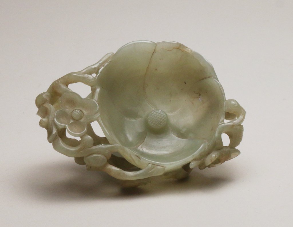 CHINESE CARVED JADE BRUSH-WASHER: of pale-green color depicting a lotus flower surrounded by stems and other flowers, h. 1 ½” w. 4 ¾” d. 3 ½”, with a near-conforming carved wood stand
