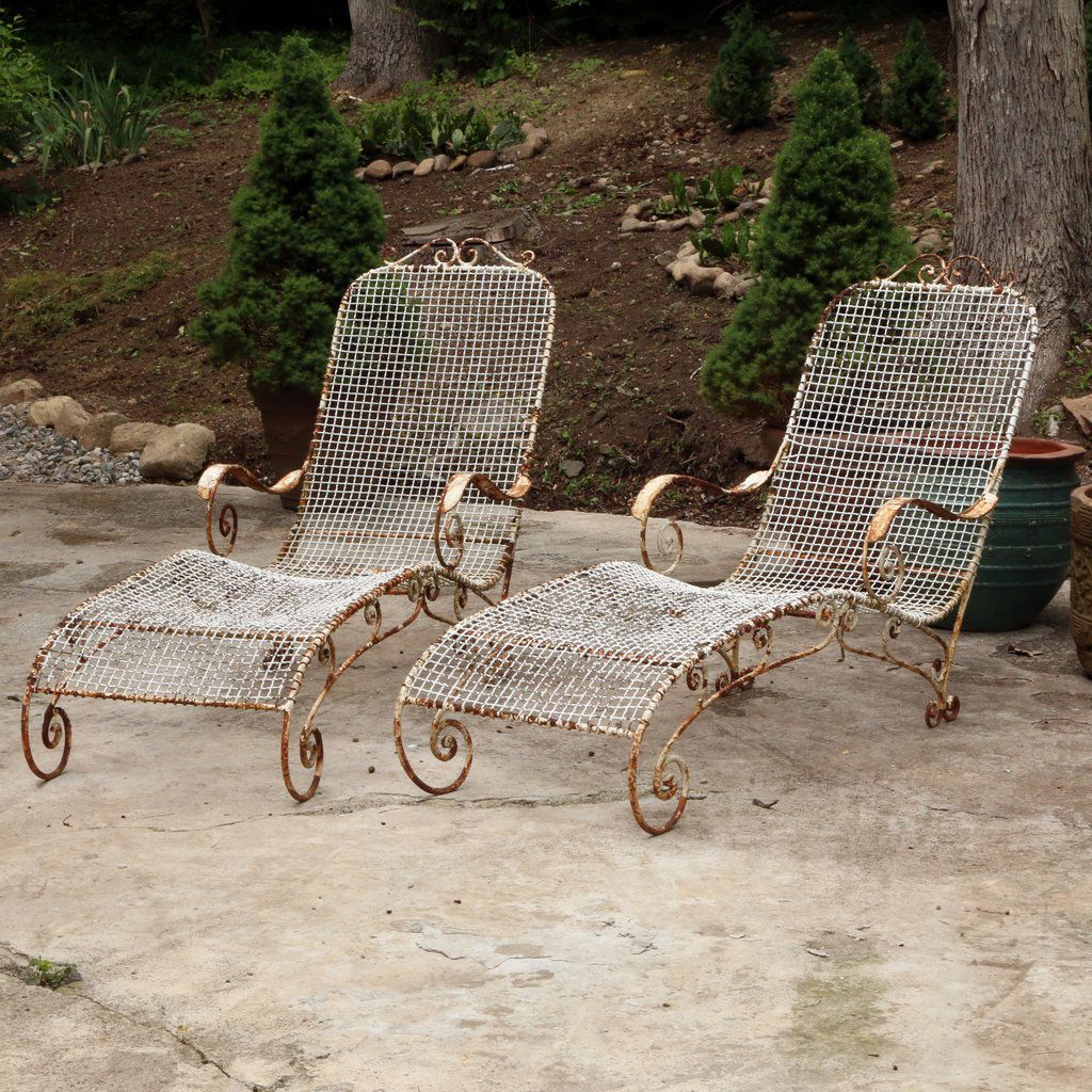 PAIR WROUGHT IRON CHAISE LOUNGES: Early 20th century, with scrolled arms and sides, old white paint with areas of rust.