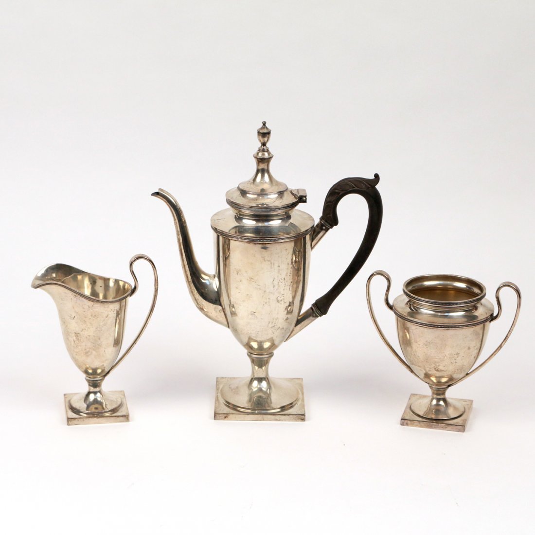 J. E. CALDWELL STERLING SILVER COFFEE SERVICE: By J.E. Caldwell & Co., Philadelphia; pattern # 781; Including a coffe pot with ebony wood handle, h. 11-3/4 in.; A trophy cup shape open sugar and a helmet shape creamer; tot. weight appx. 28 toz.