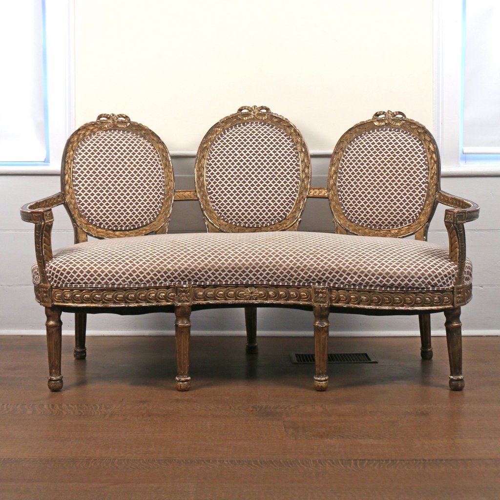 NORTH ITALIAN GILT CARVED TRIPLE-BACK SETTEE: NORTH ITALIAN GILT CARVED TRIPLE-BACK SETTEElate 18th/early 19th Century, in the neoclassical style with three laurel-carved backrests above a kidney-shaped seat with conforming arms, the ‘strung-co