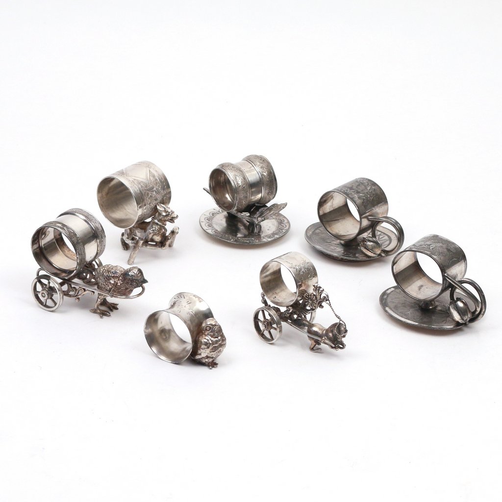 (7pc) FIGURAL SILVER-PLATED NAPKIN RINGS: (7pc) FIGURAL SILVER-PLATED NAPKIN RINGSIncluding two in lily pad form, one with a small chiclet, one with a bird drawing a cart, another with a horse drawing a cart (front legs with damage), one with