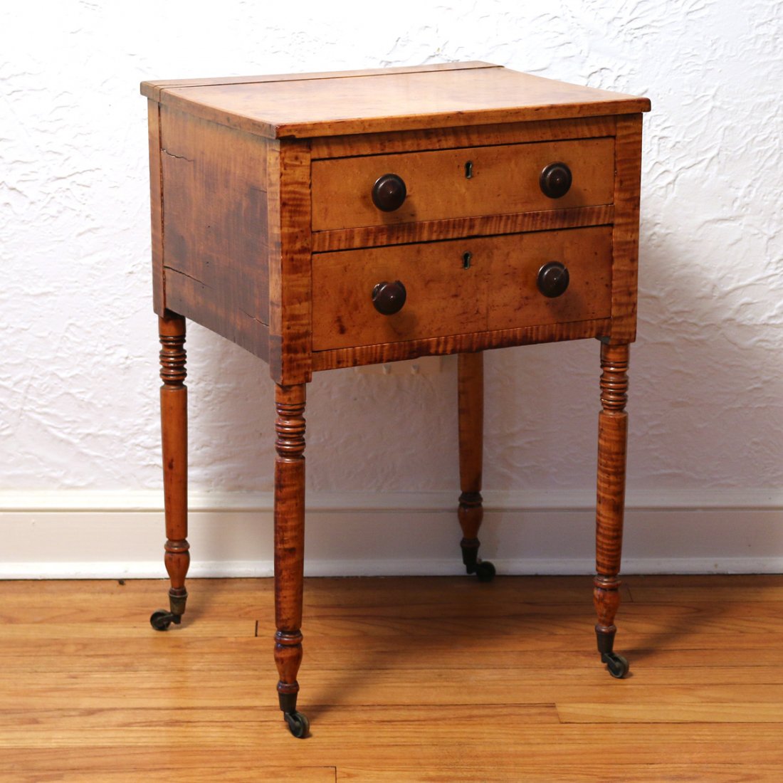 SHERATON SOLID FIGURAL MAPLE STAND: early 19th Century, having two drawers with original turned wooden pulls, round turned legs on casters, h. 28 in., w. 19 in., d. 16 ½ in.