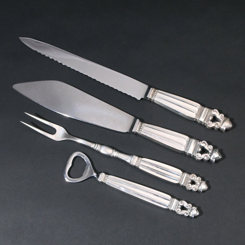 (4pc) GEORG JENSEN SERVING UTENSILS: In the acorn pattern including a bottle opener, a carving fork, a fish server, and a bread knife (l. 11-1/4in.)