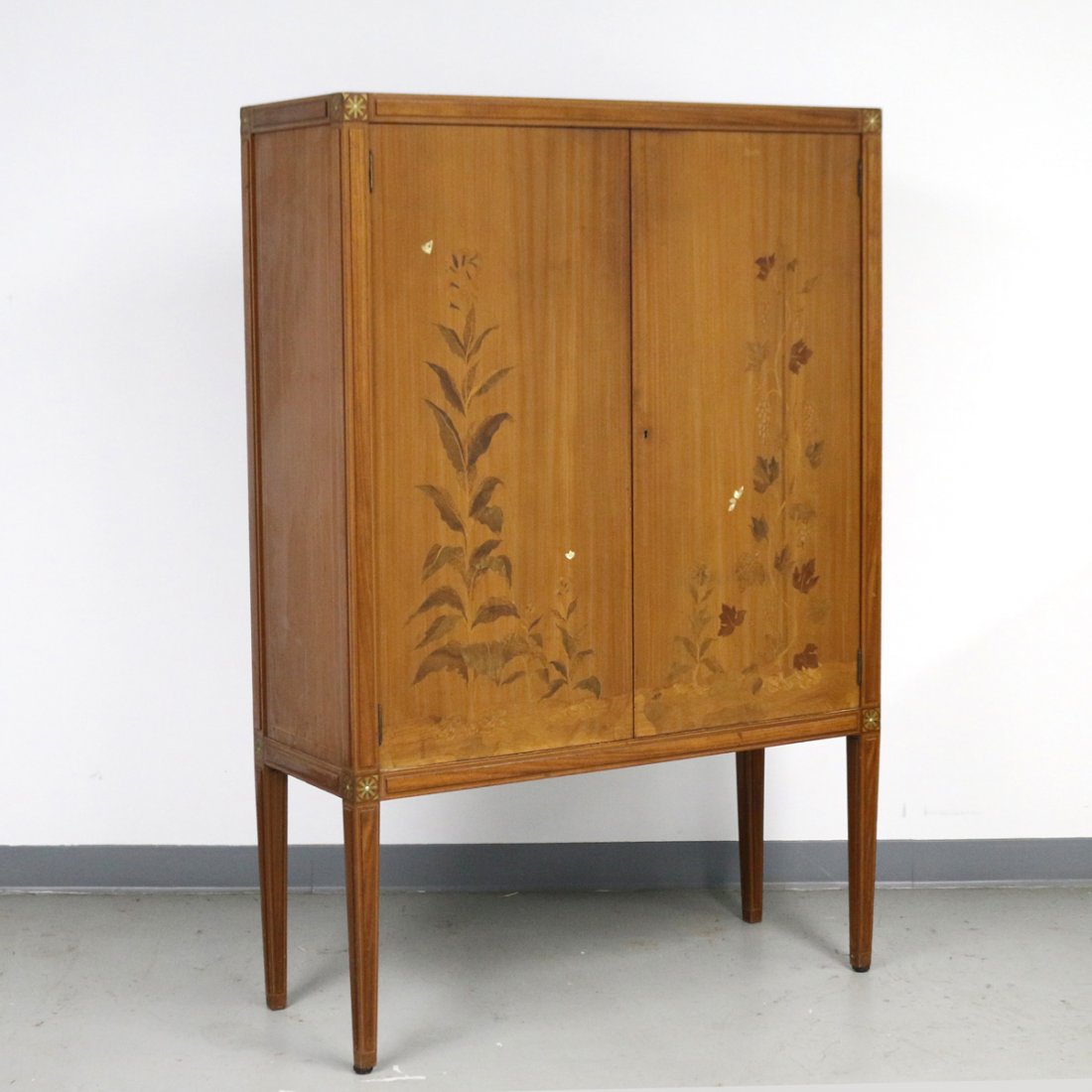 ART DECO INLAID BAR CABINET: Having full-length double doors with inlaid plants and mother of pearl insects, raised paneled stiles with inlaid metal and contrasting woods forming flower heads at the corners, interior door side de