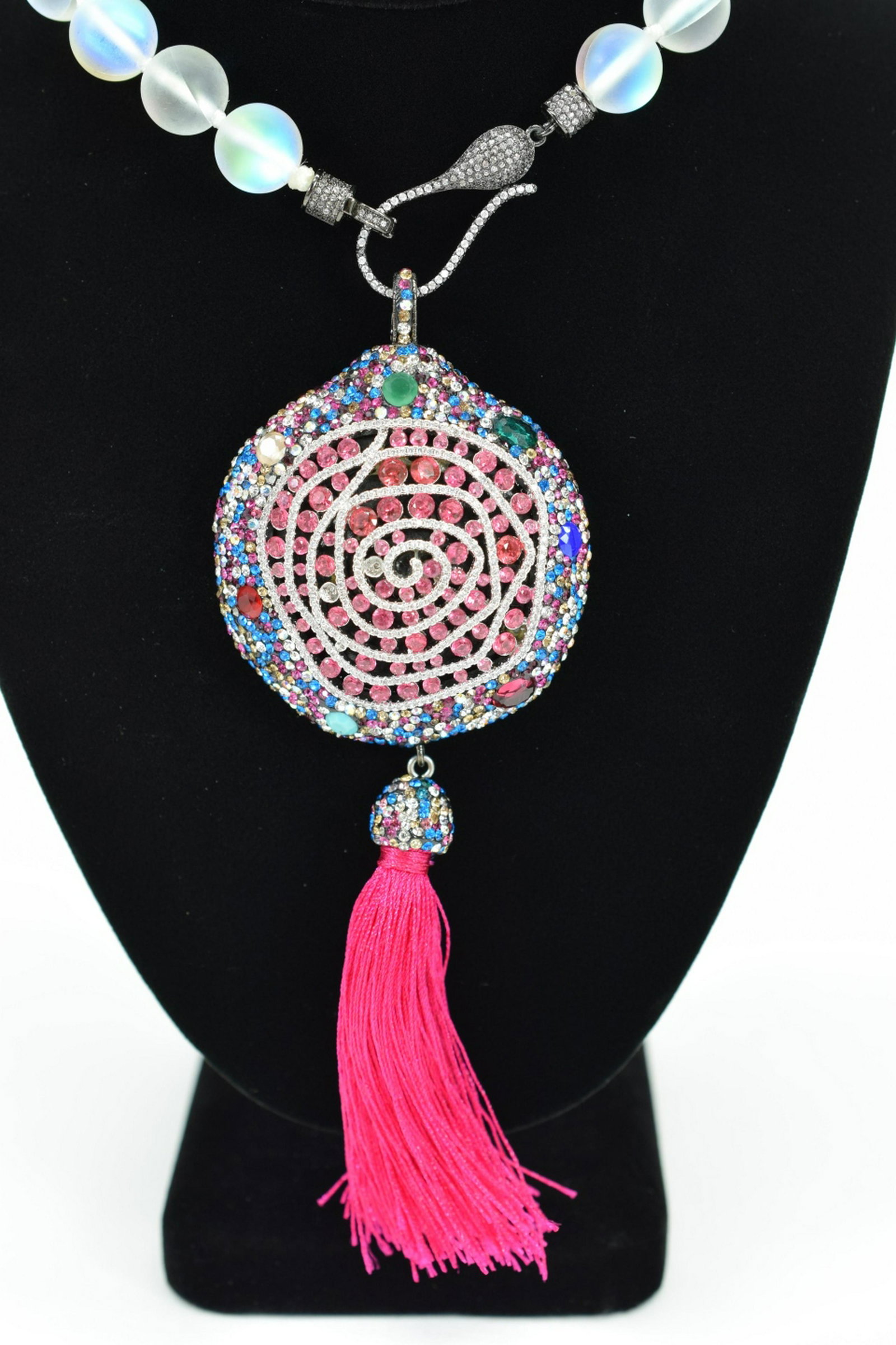 IRRIDESCENT GLASS BEAD NECKLACE & BLING PENDANT: Costume fashion Mystic Aura beaded necklace with a multi-colored rhinestone encrusted pendant having pink silk tassels. Measures approx. 19" L (plus 6" L pendant with tassels). Weighs 126.4g. U.S. SHI