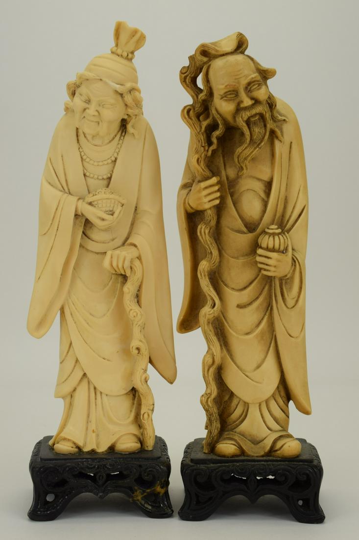 PAIR FAUX BONE ASIAN CARVED ELDER FIGURES ON BASE: Vintage pair of carved faux bone figures depicting an elderly couple, each with their own walking stick. Each measures 8-1/2' H atop a 1-1/2" H matching carved wooden bases (approx. 10" H overall). To