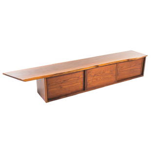 George Nakashima walnut wall-mounted cabinet: signed and dated June 1983; beveled edge on overhanging top, three compartments enclosed by sliding doors, dovetailed joinery, 18 in. H., 104 in. W. 18 in. D.