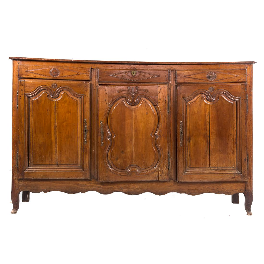 Country French Carved Fruitwood Buffet: late 18th century; flat top with canted corners and molded edge, three drawers in apron, three compartments with shelves enclosed by carved panel doors, shaped apron, cabriole legs, 46 in. H., 74 in. 
