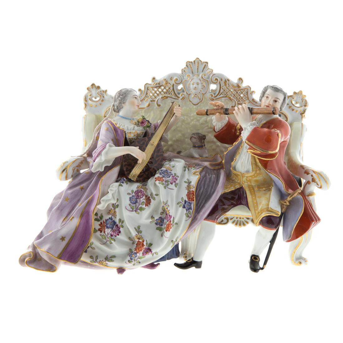 Meissen Porcelain Figural Group: late 19th century; underglaze blue crossed swords mark, inscribed/incised "W56/40," depicting a couple seated on a sofa and playing instruments with a small dog between them, 6 in. H., 9 in. L.Estate