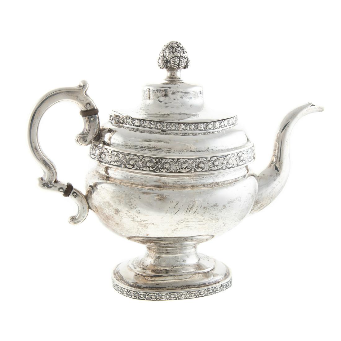 American Coin Silver Teapot: John Wesley or John Wolfe Forbes, New York, c. 1808-1838; oblong form, on a pedestal foot, the neck, shoulders and foot with floral border, floral urn finial, with c-scroll handle, one side with chase