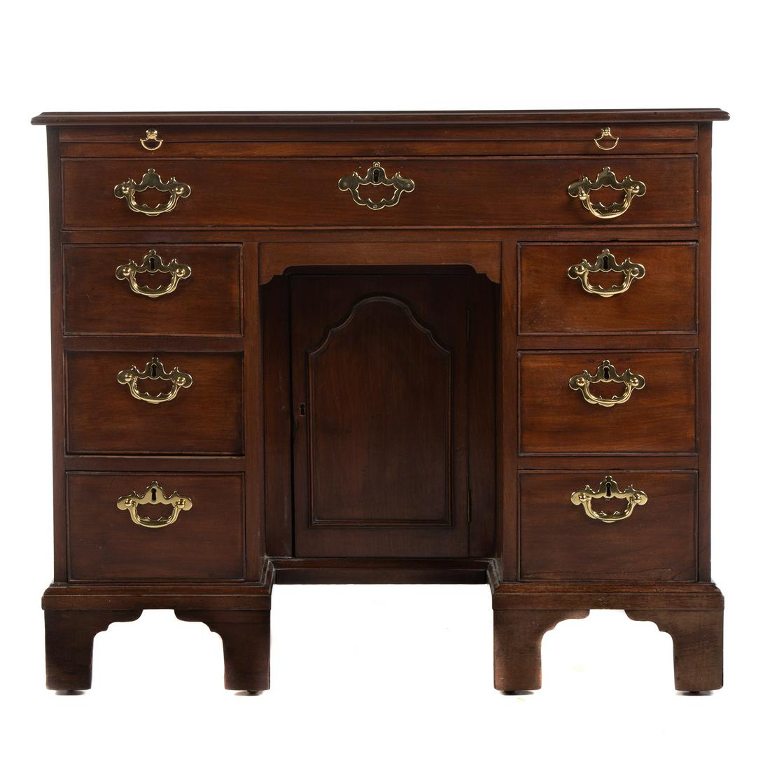 George III Mahogany Kneehole Bureau Table: Late 18th century, flat top with molded edge, brushing slide and long center drawer, three short drawers to each side of recessed knee hole compartment with compartment enclosed by solid panel door, s