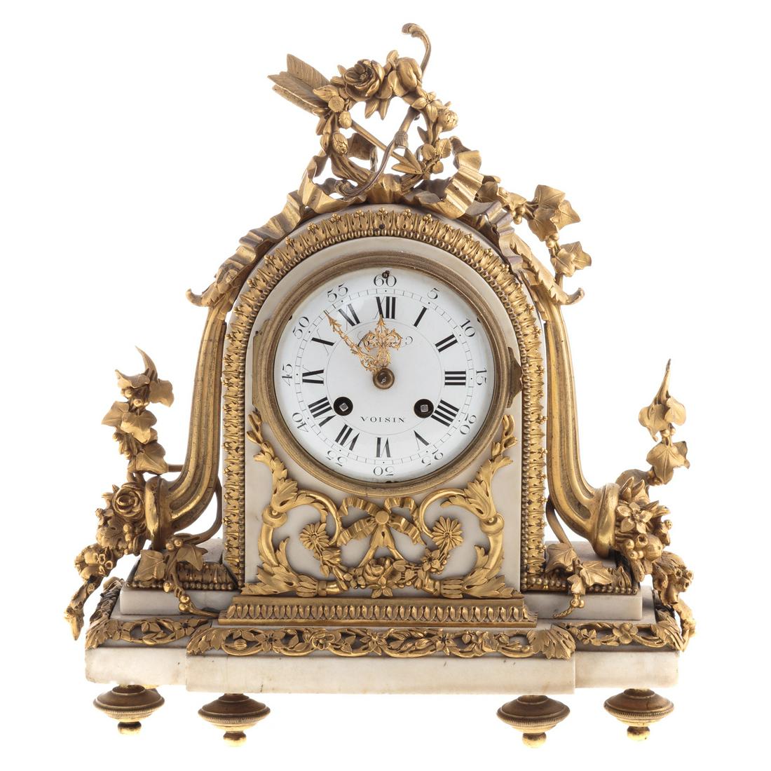 French Rococo Marble & Ormolu Mantle Clock: Circa 1760; carved white marble case with ormolu cornucopia, floral and ribbon mounts, enamel face marked "Voisin,' on bronze feet. 13 in. H., 11 in. W.