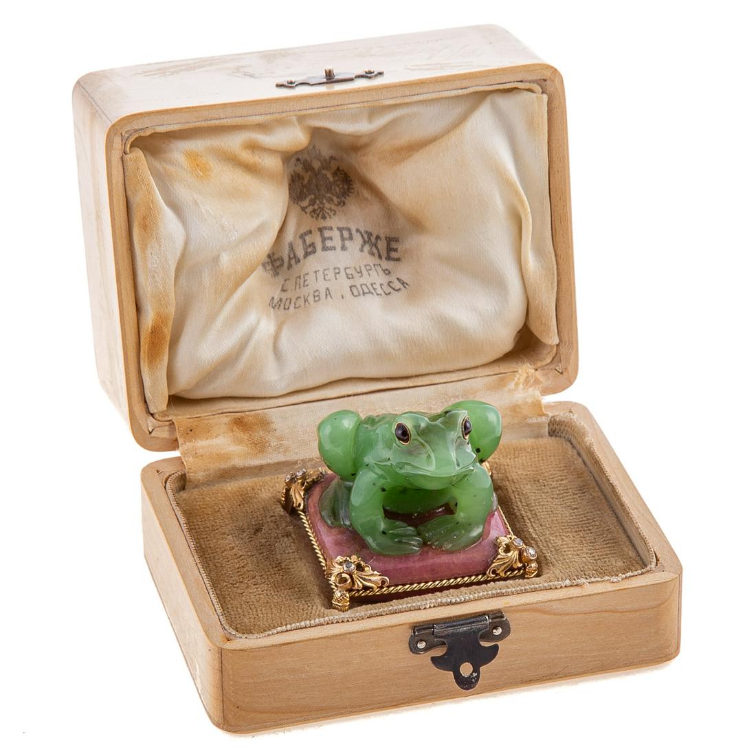 Russian Carved Nephrite Frog: In the Faberge manner, small frog seated on mineral pillow, with gold frame and inset jewels on corners, 1 3/4 in. H., 1 3/4 in. Sq., in felt and velvet lined Faberge style wood box.